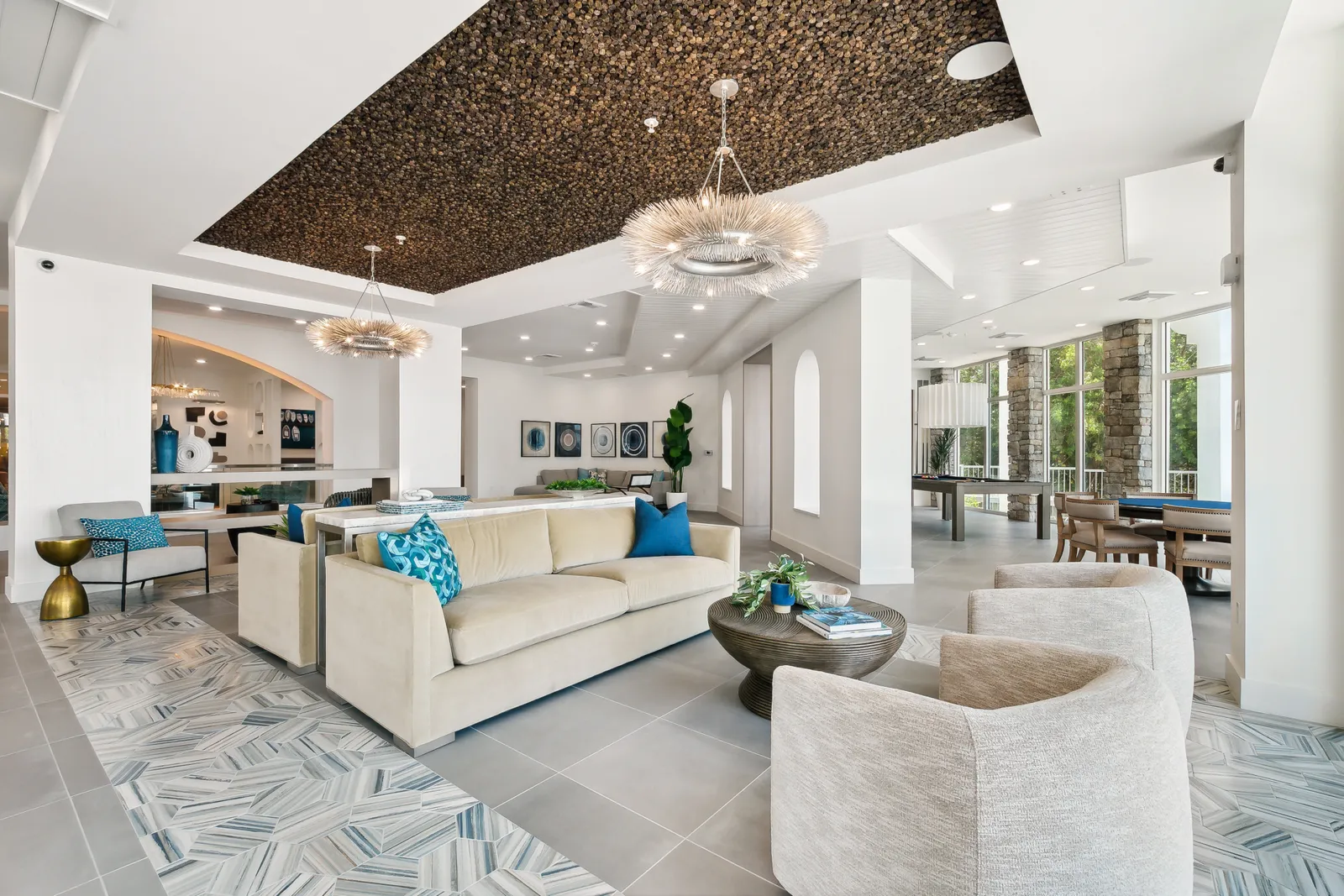 A room with couches, chairs, and pendant lighting, all in shades of white and brown.