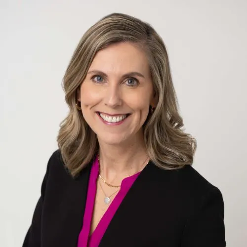 Stacy Hurt smiling in a black blazer and magenta blouse against a light background.