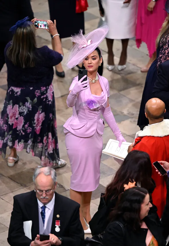 A woman in a lilac corset dress and plate-sized hat takes selfies in Westminster Abbey.