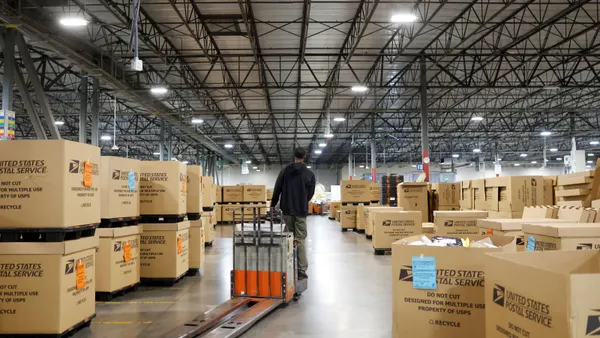A person stands next to a machine in a warehouse surrounded by boxes.