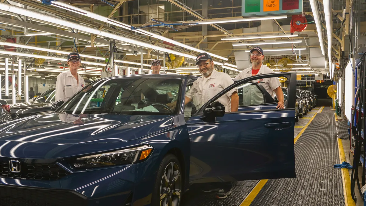 Workers at Honda of Canada Manufacturing in Allison, Ontario pose with a 2025 dark blue Civic hybrid during its production start in June 2024.