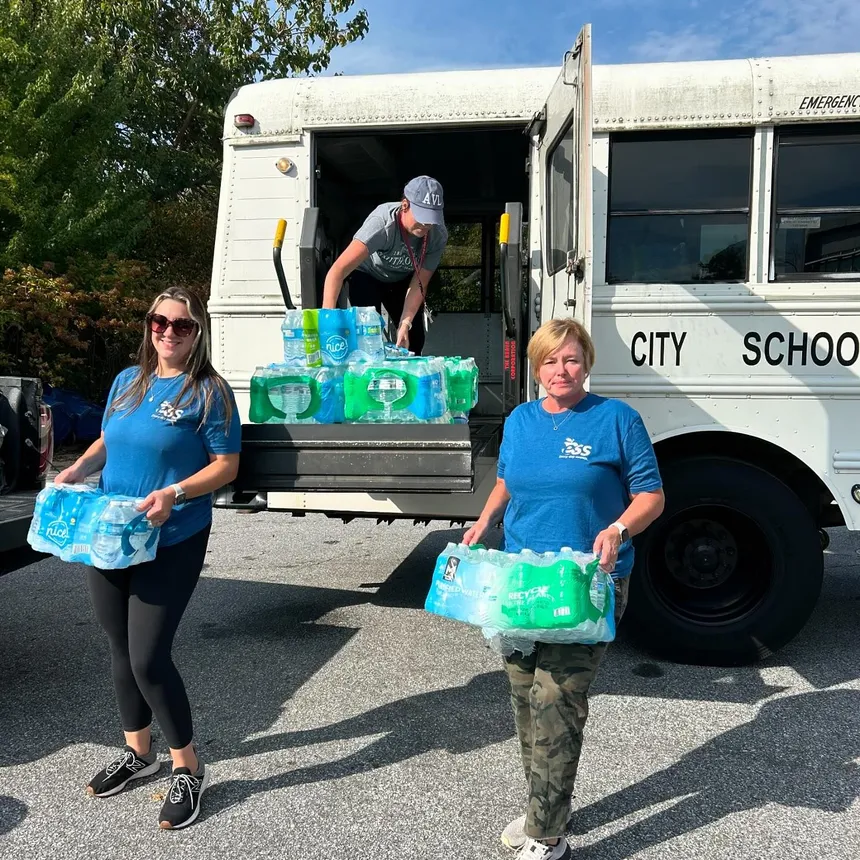 Three individuals load cases of water off of a school bus