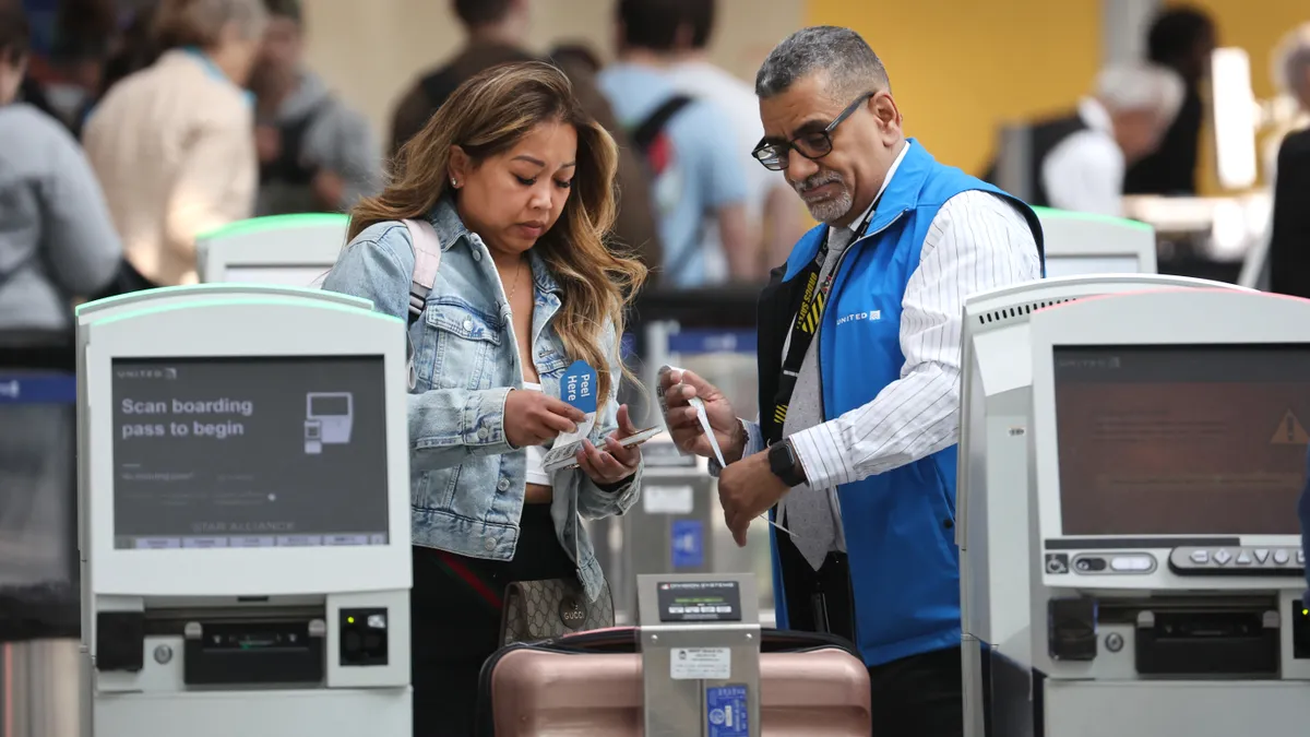 An employee aids a customer in attaching a tag to their luggage.