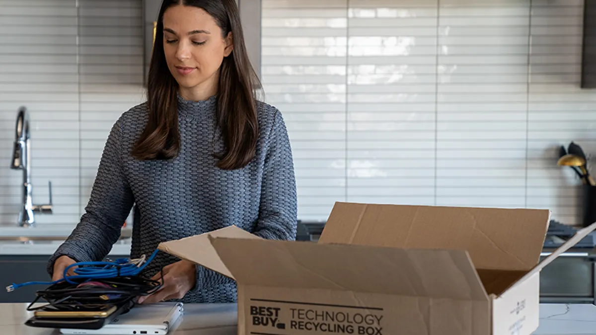 Person grabs old technology to put in a tech recycling box that is on a counter.