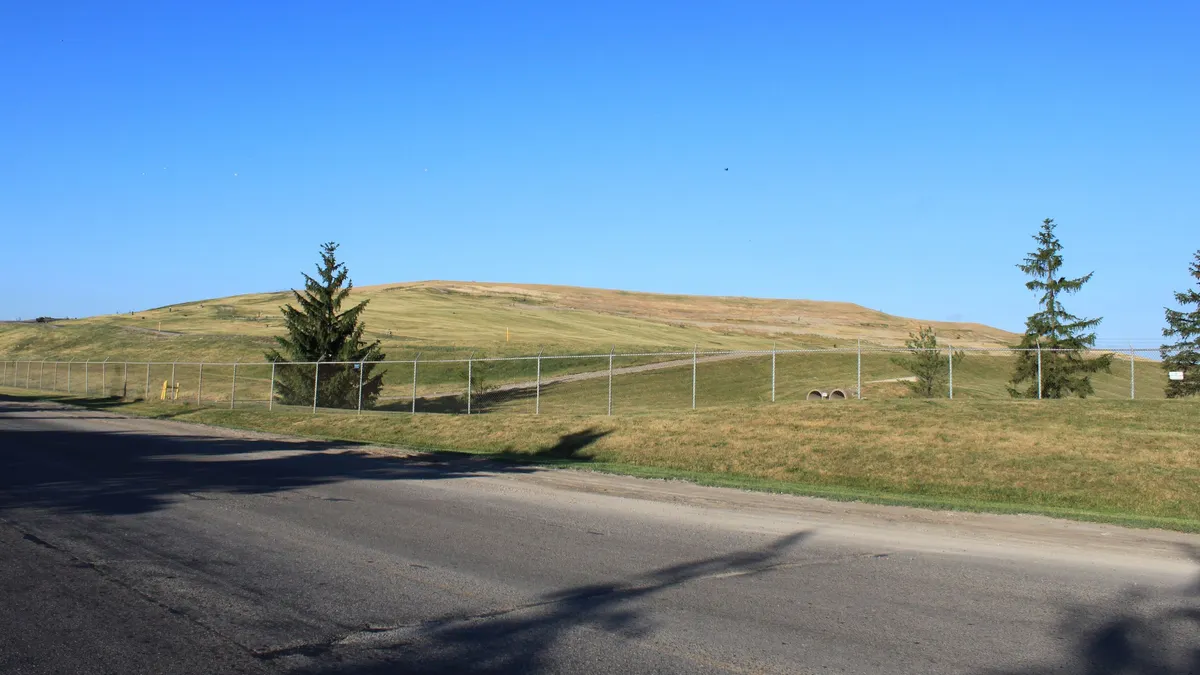 Image of a large mound covered in grass taken from a road.
