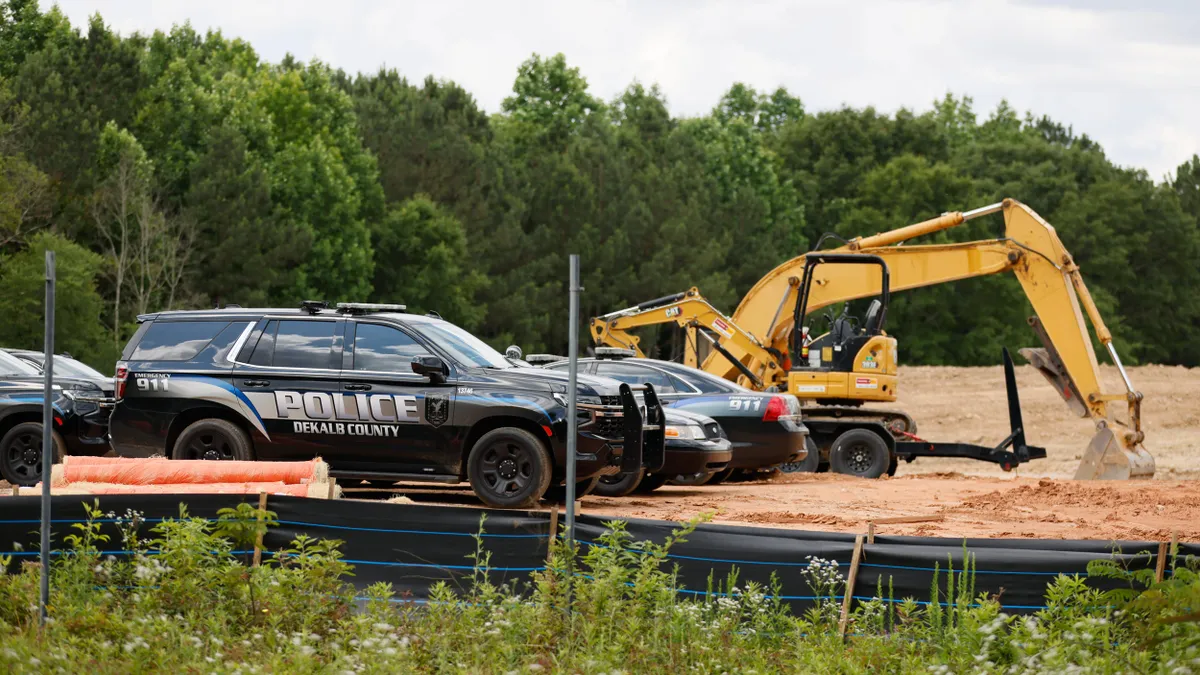 Police vehicles sit parked in front of construction vehicles on a jobsite.