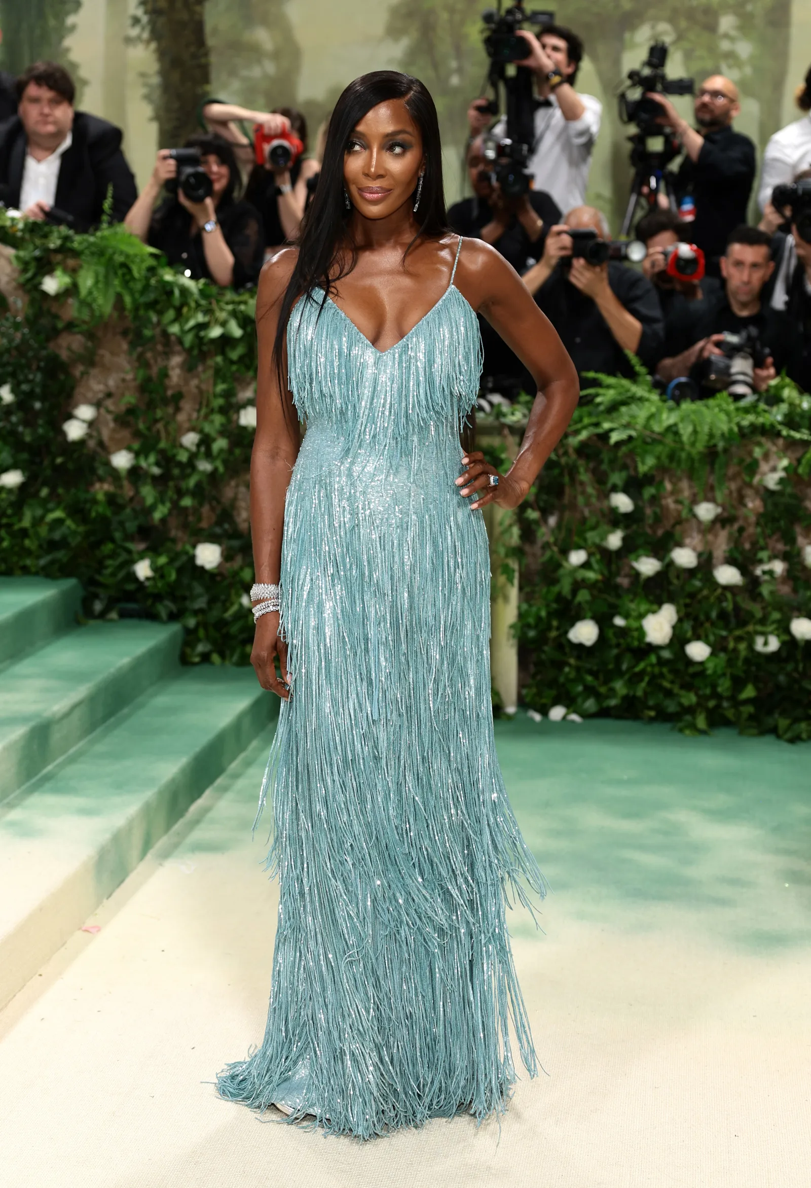 A woman in a baby blue fringed gown stands in front of photographers.