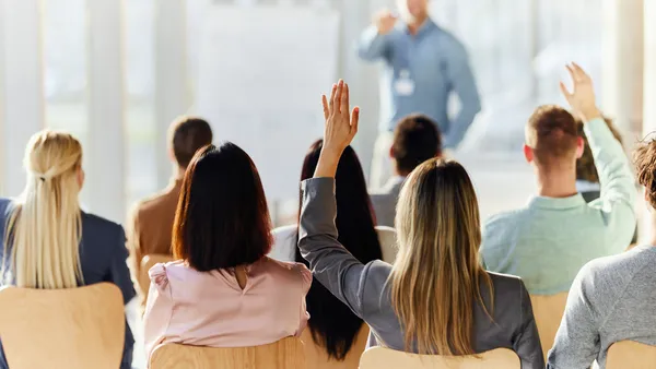 Rear view of a people raising their hand to ask a question at a work event in the board room.