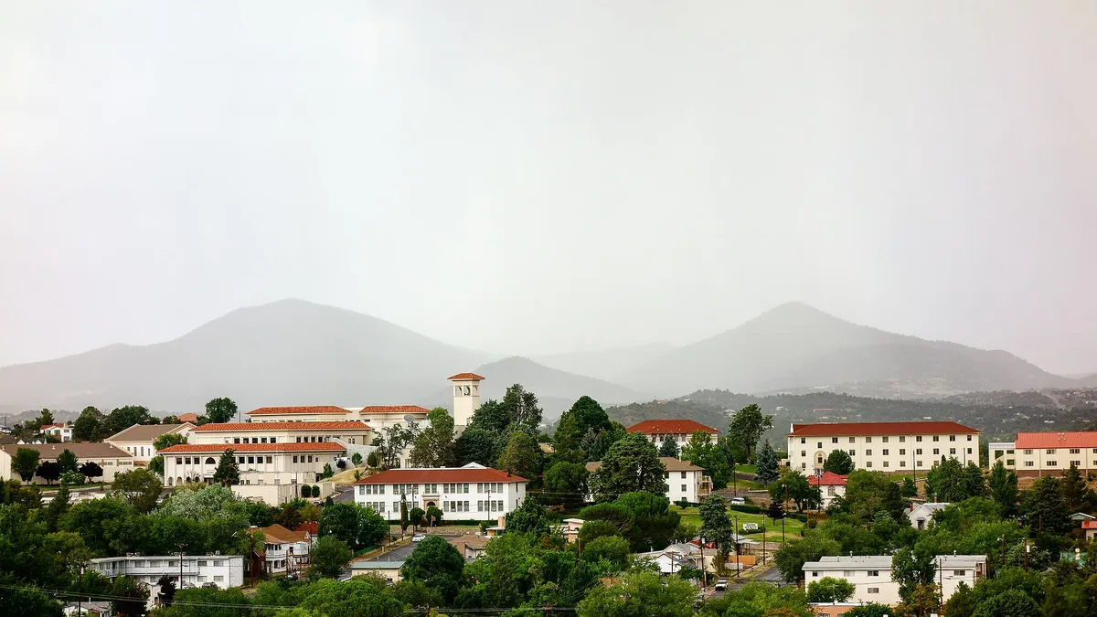 Campus with red tile roofs and white stucco buildings against backdrop of mountains.