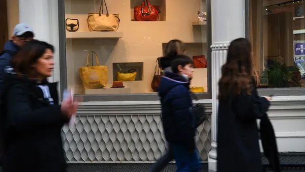 A group of people shopping walk quickly past a store window displaying luxury handbags.