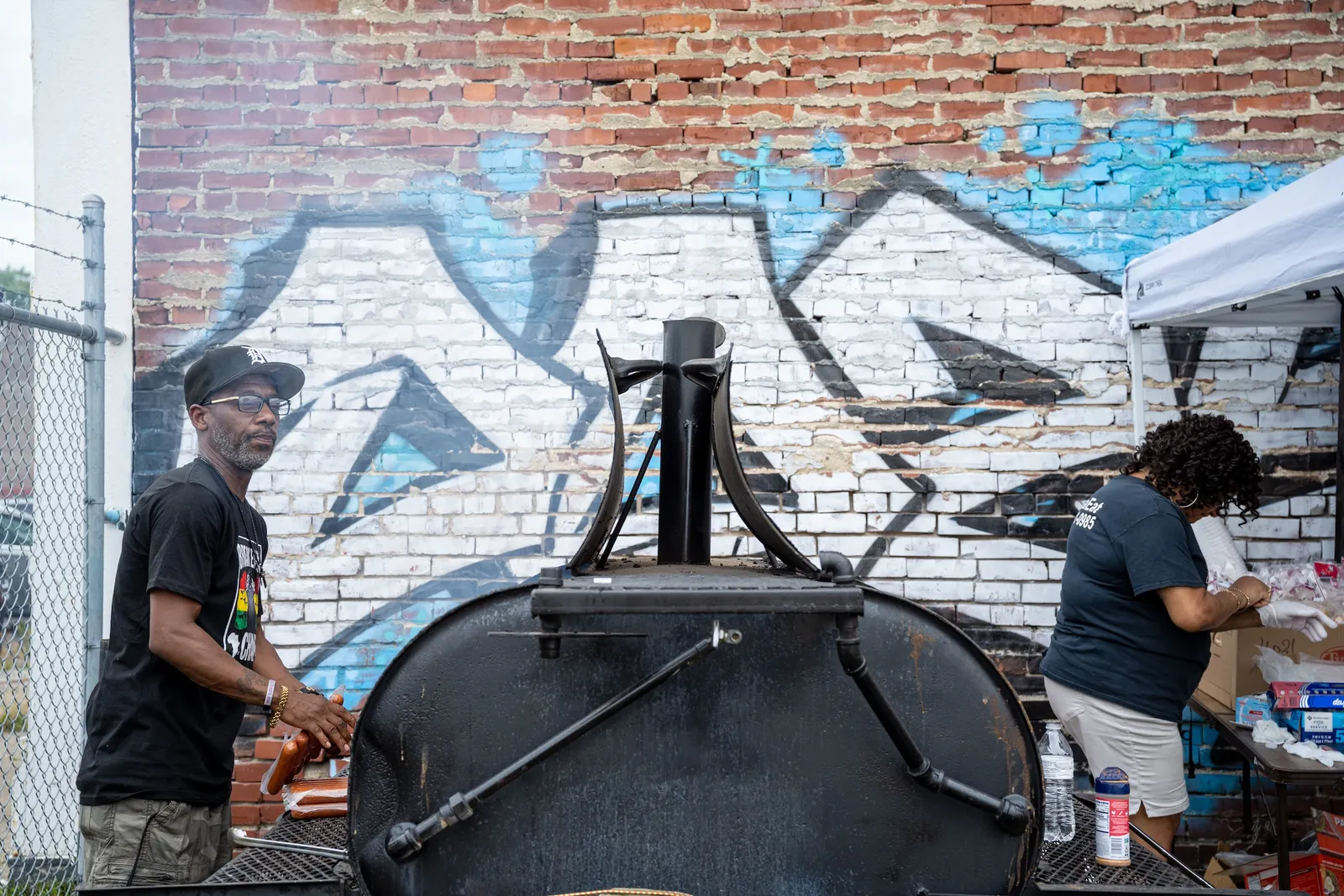 A person next to a barbecue grill in front of a brick wall