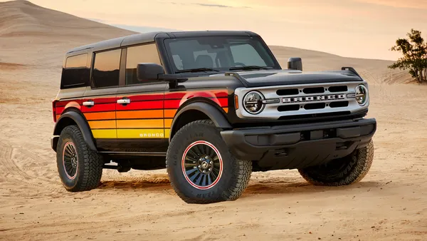 A 2025 Ford Bronco with the Free Wheeling appearance package with orange, red and yellow striping on the sides parked outdoors on a sand dune.