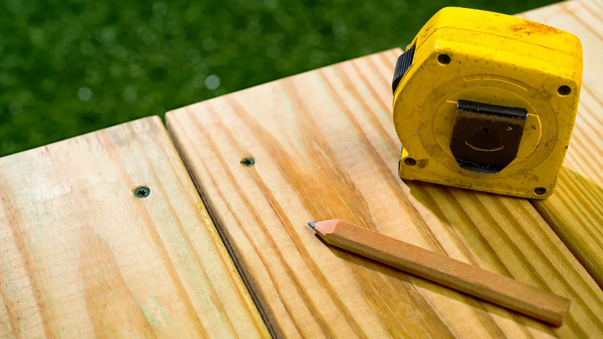 A tan pencil and yellow measuring tape sitting on a newly contructed outdoor deck.