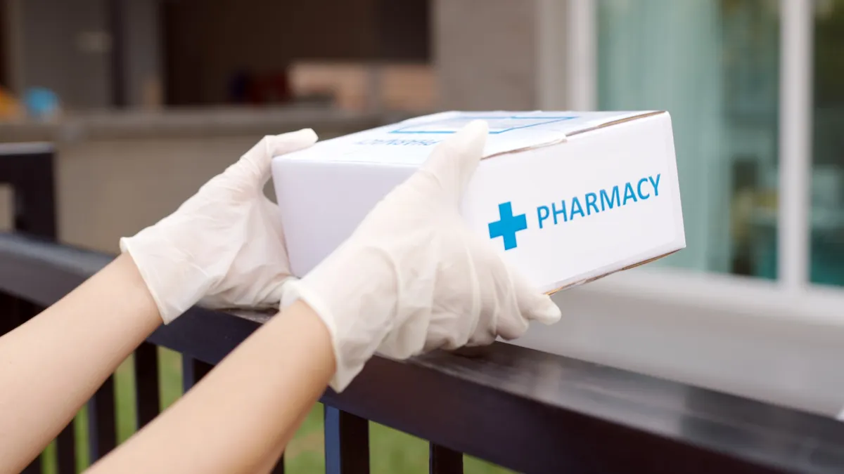 Person wearing latex gloves delivers a pharmacy package over a fence.
