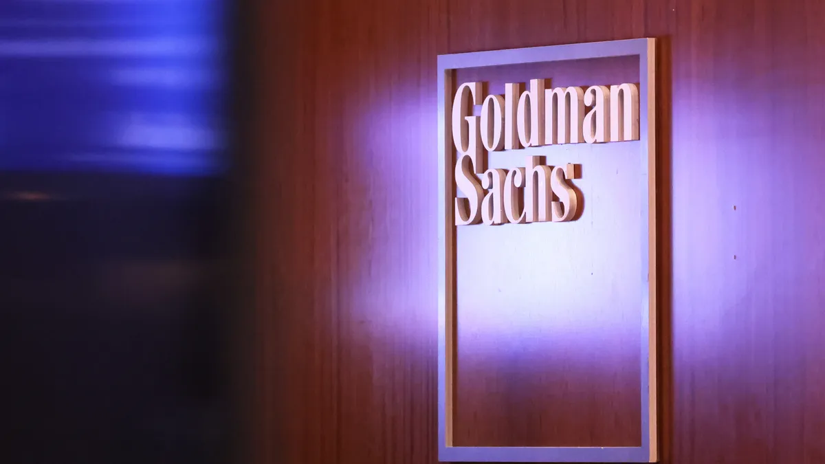 A sign reading Goldman Sachs is seen on a wood-grained wall.