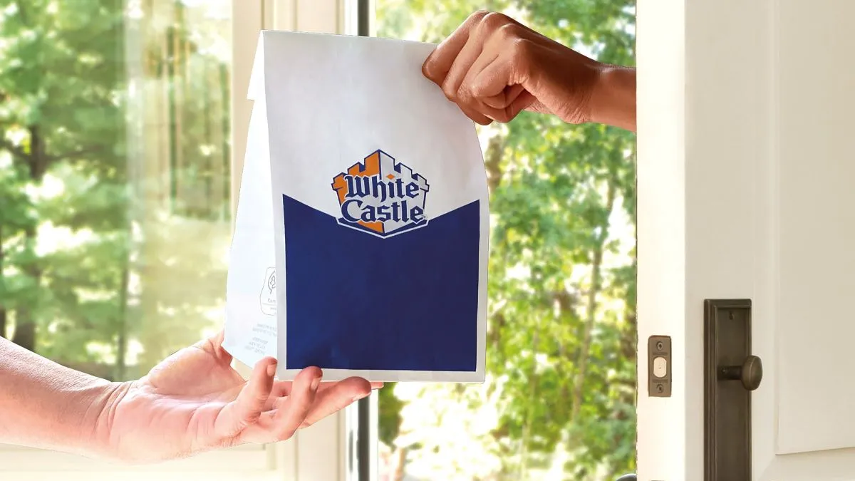 A hand receives a White Castle bag from another hand coming from outside the door