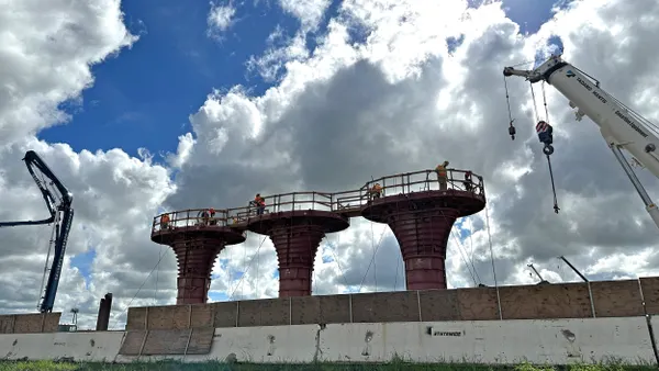 Construction workers high up on large pedestals with cranes nearby.