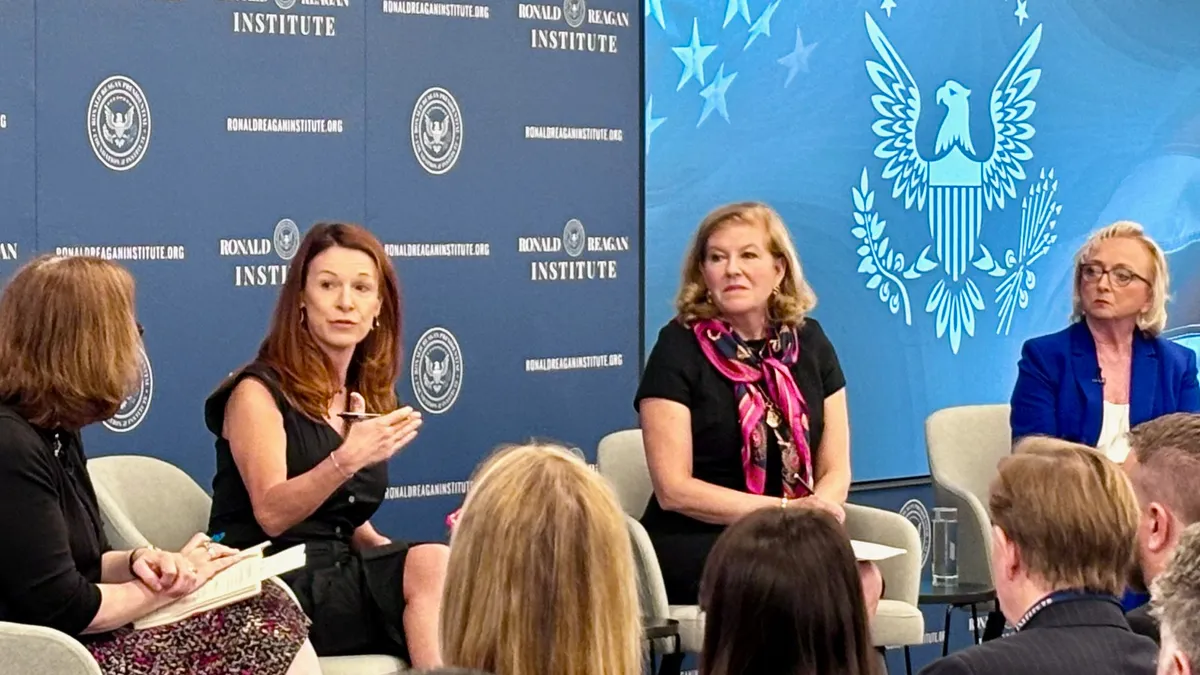 Four people sit in chairs on a stage in front of rows of people. Behind them is a blue wall with white writing