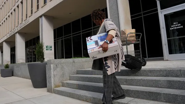 A person is carrying a box while walking down the stairs in front of the outside of a federal building