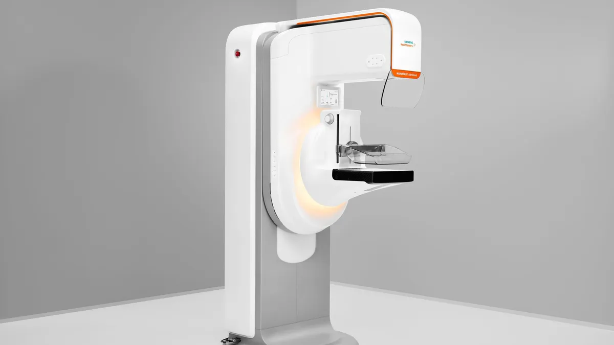 A white and gray mammography machine is in an empty room.