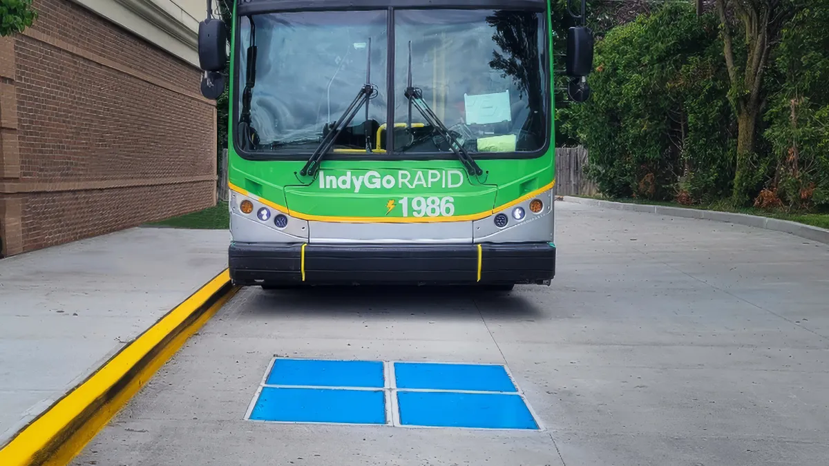 A green IndyGo transit bus pulls up to an inductive electric charging pad.