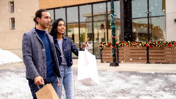 Two people walking down snowy sidewalk holding shopping bags