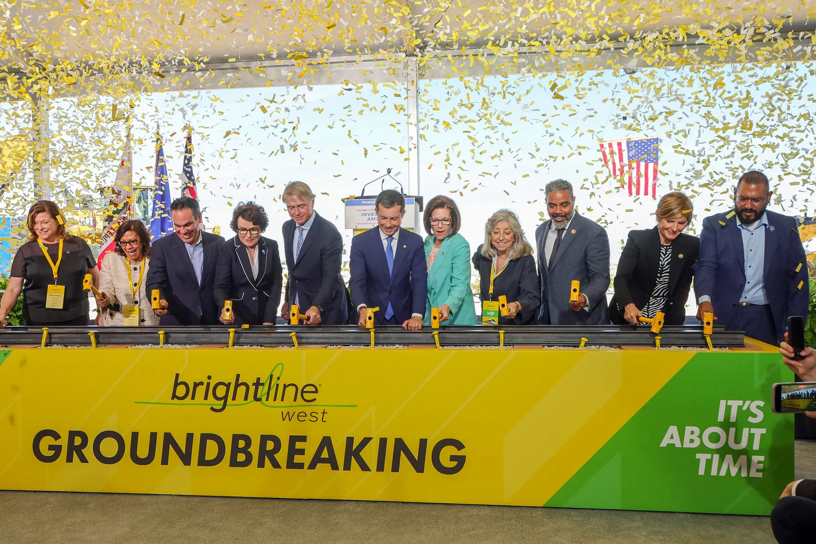 Large group of men and women at a table with confetti flying above them. Sign on table reads Brightline West.