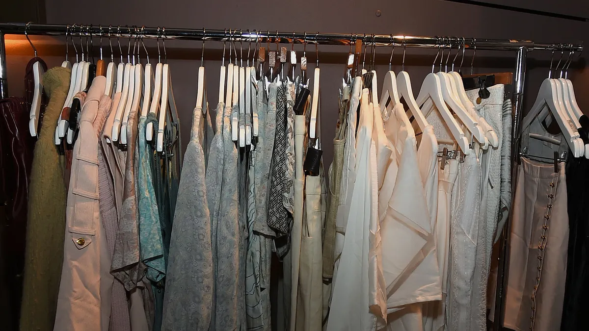 Various pieces of apparel is seen on a clothing rack, hanging by hangers.