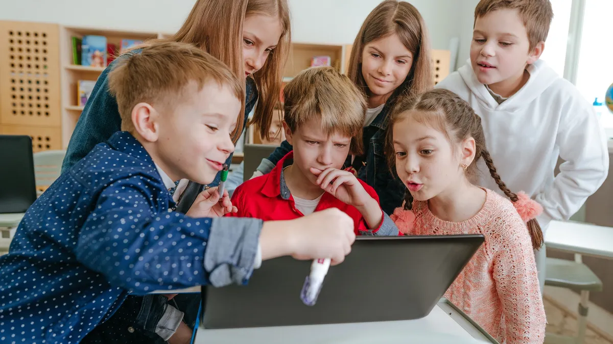 Kids in classroom collaborating on tablet.