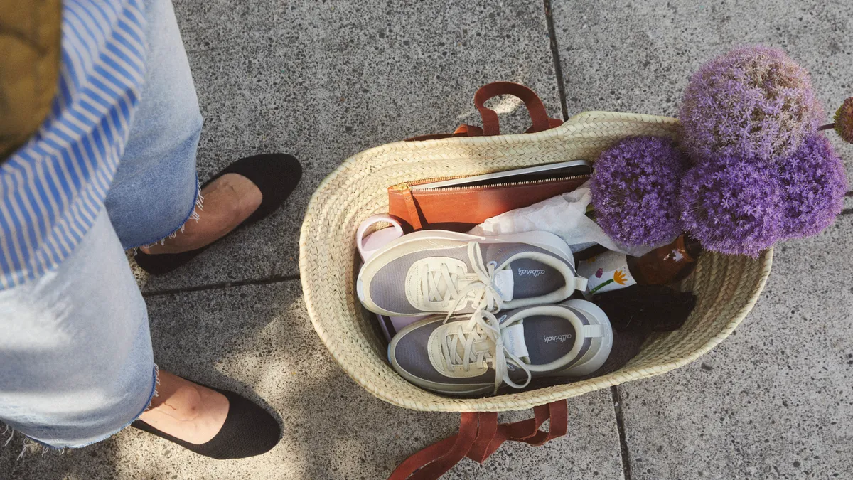 A pair of grey Allbirds sneakers sit inside a straw basket on a sidewalk