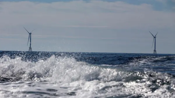 Wind turbine seen in the distance beyond crashing waves