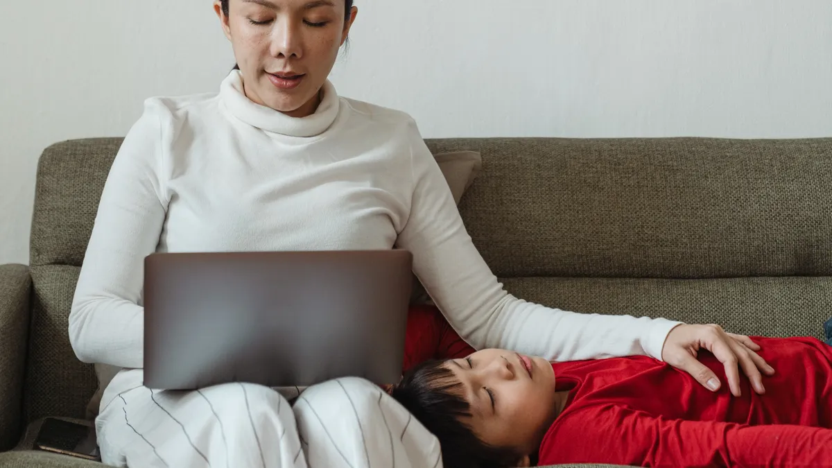 An Asian person works and their kid jumps on the table