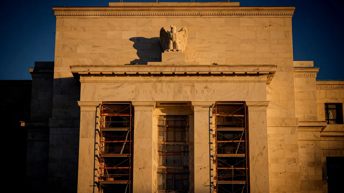 The sun sets on a white stone building that features an eagle sculpture atop a series of columns. Scaffolding is seen between each of the four columns.