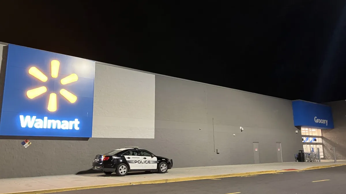 A black and white police car is parked in front of a Walmart store at night