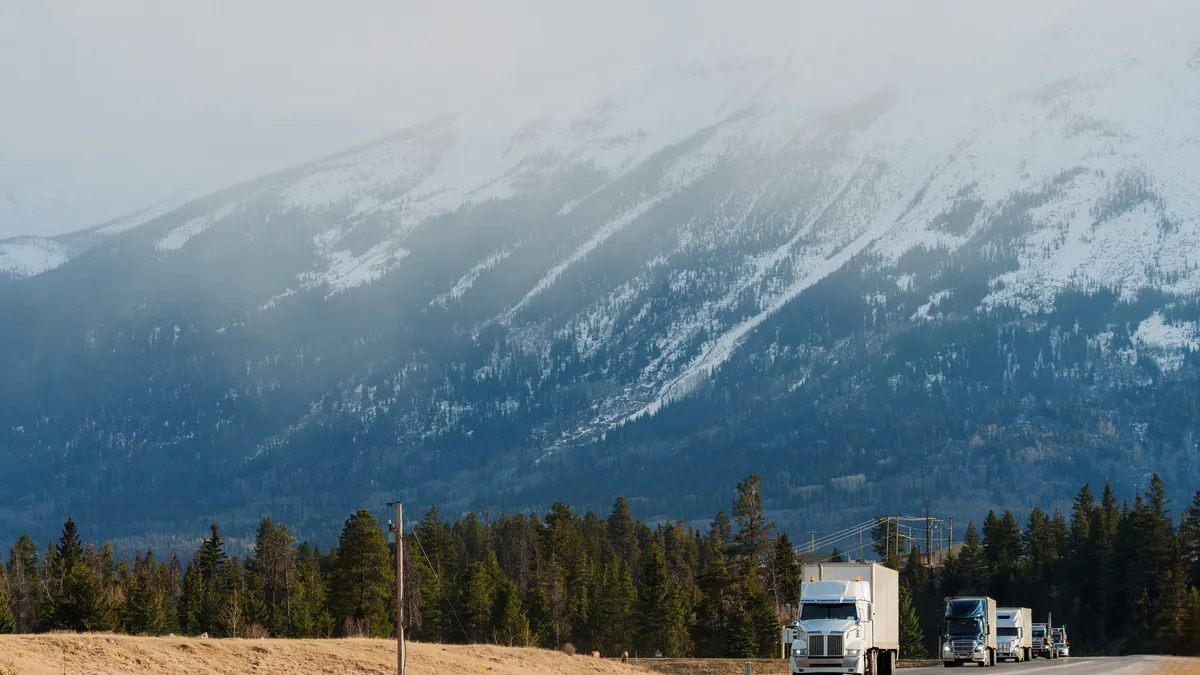 A snowy mountain in the background with trucks on a road.