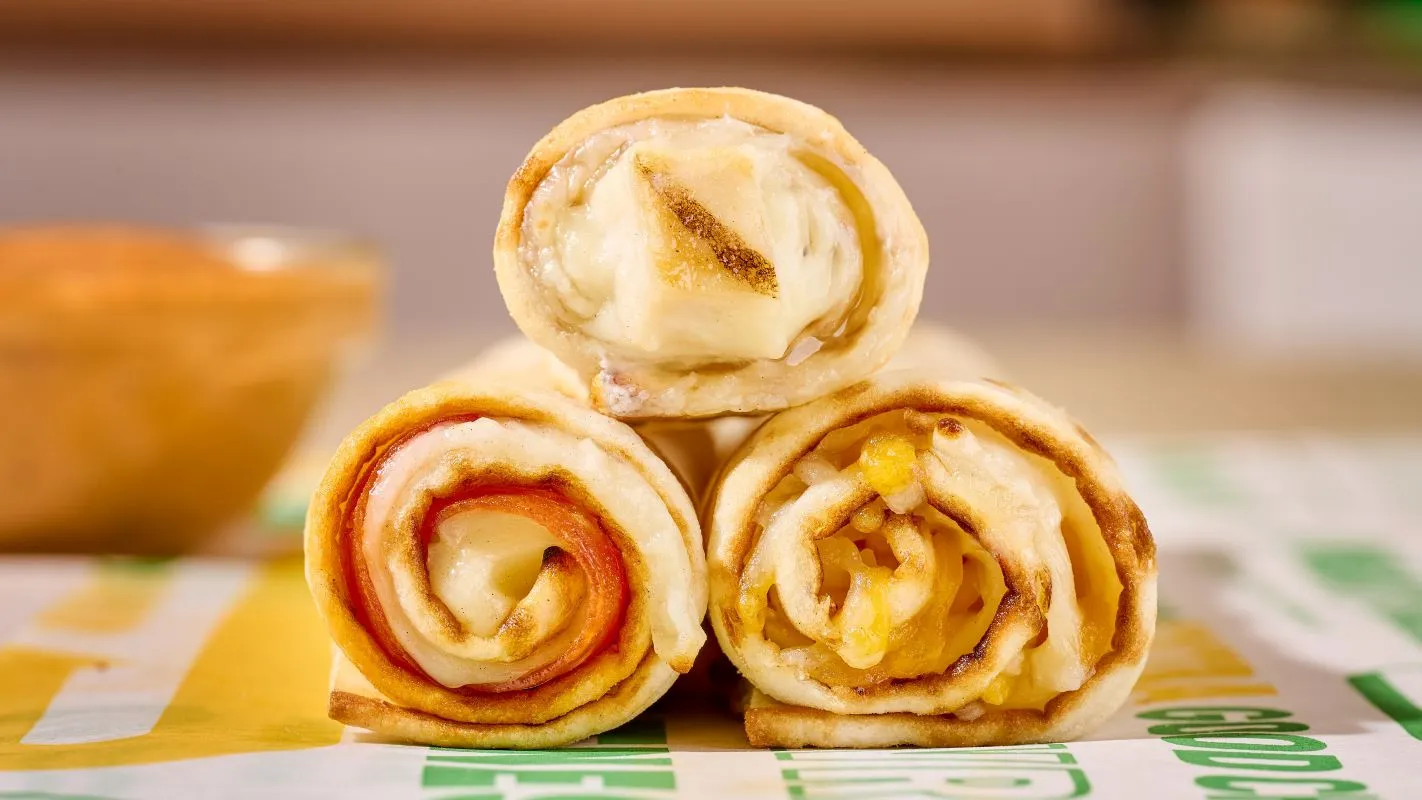 Three lavash wraps with meats inside stacked in a triangle on top of wrappers that say Subway.