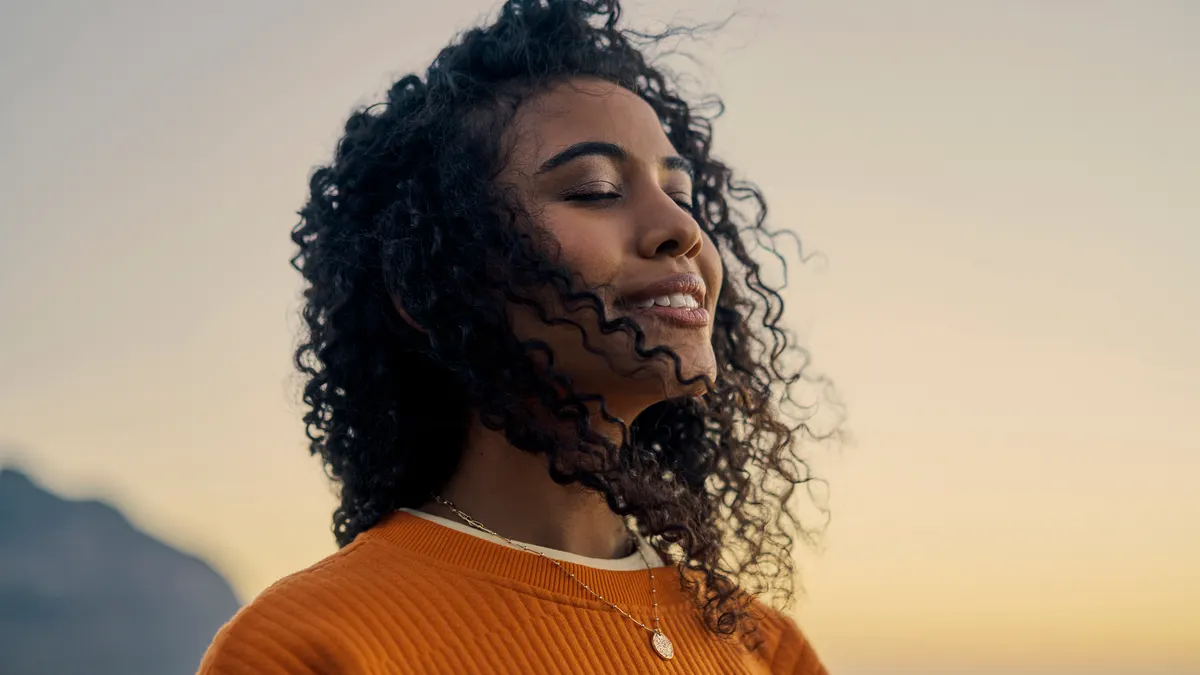 Woman in orange sweatshirt standing against a sunset