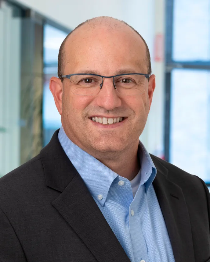 Man in a suit and glasses smiles.