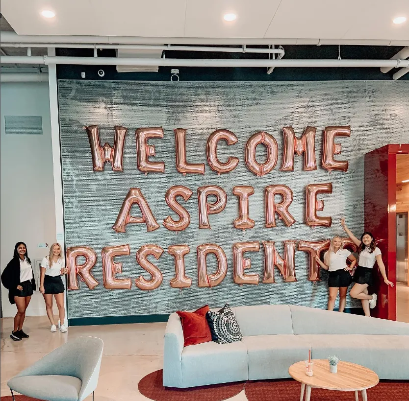 People stand beside a giant "Welcome Aspire Students signs"