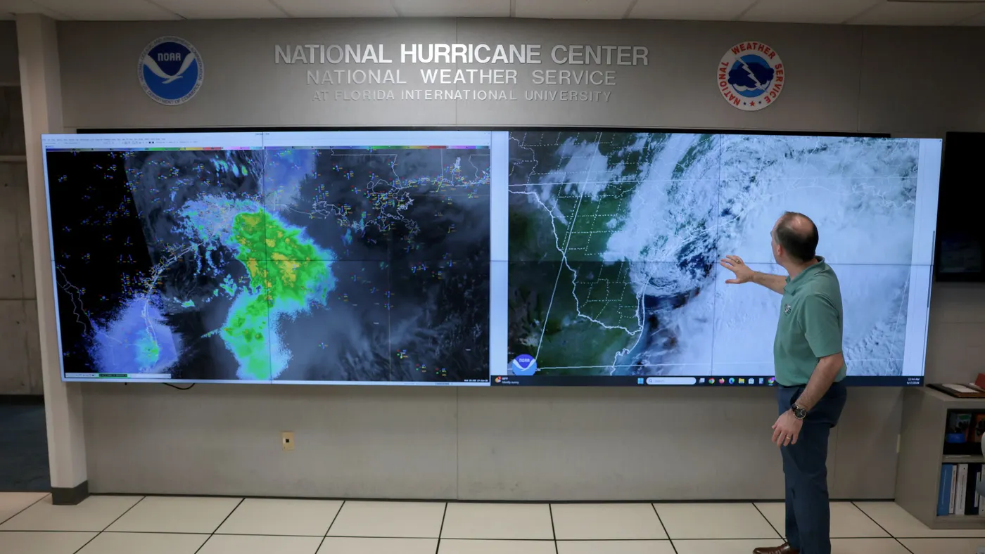 A man stands in front of large screens that show weather maps.