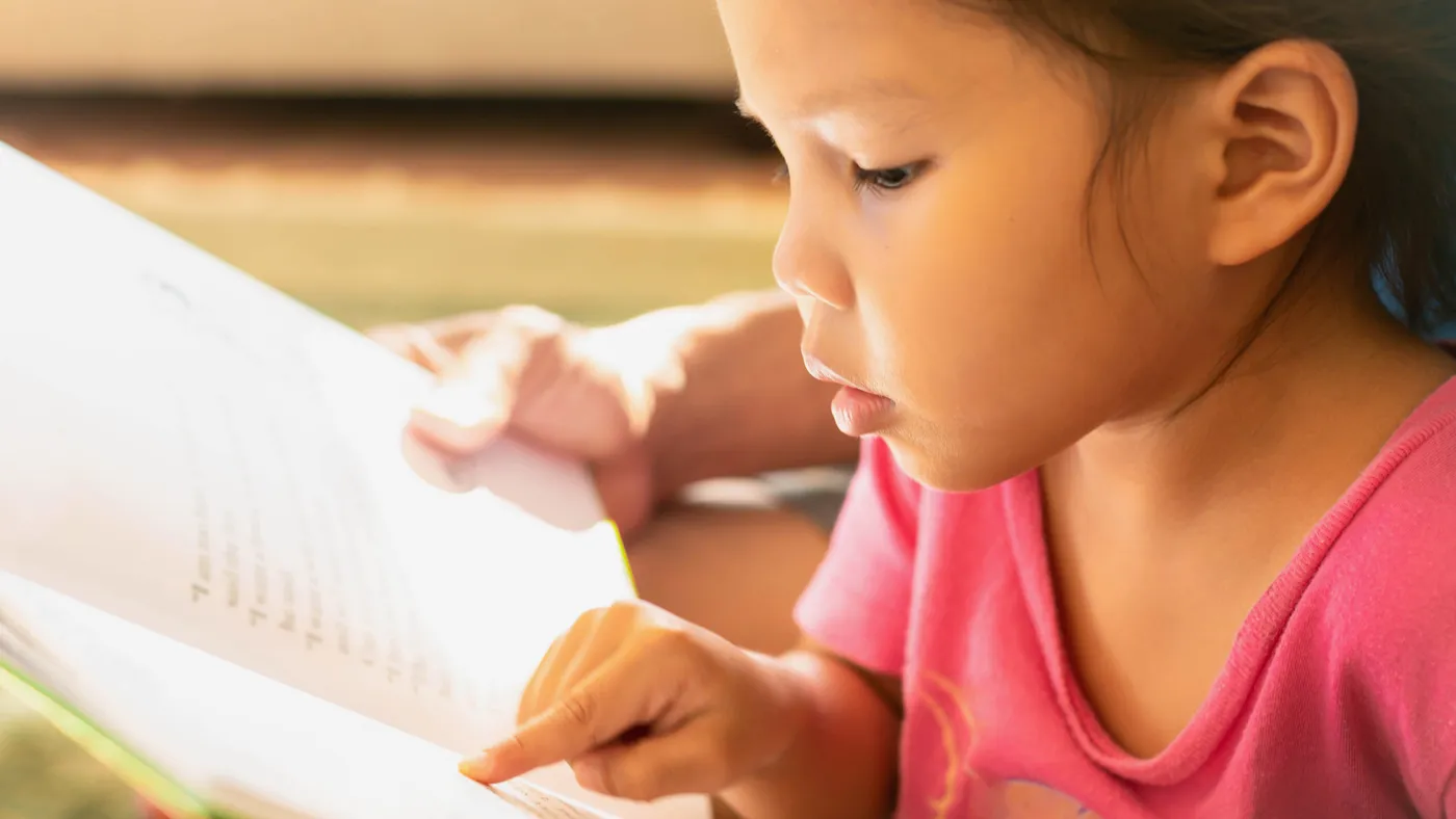 A young student points to pages in a book.