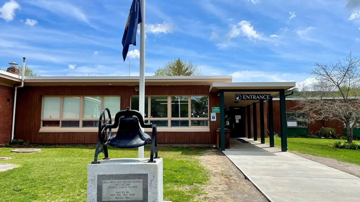 A building of the Vermont Department of Education stands behind a raised flag and bell.