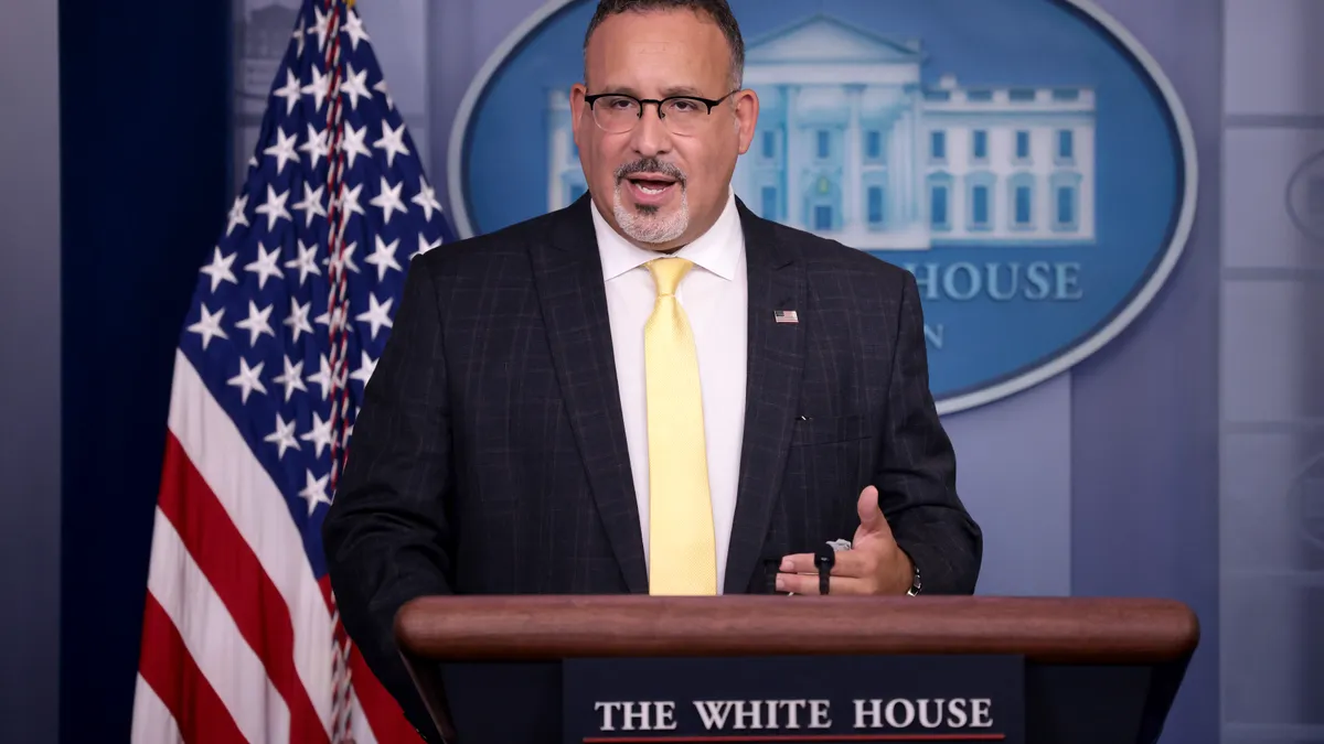 Education Secretary Miguel Cardona speaks at a podium in the White House press briefing room.