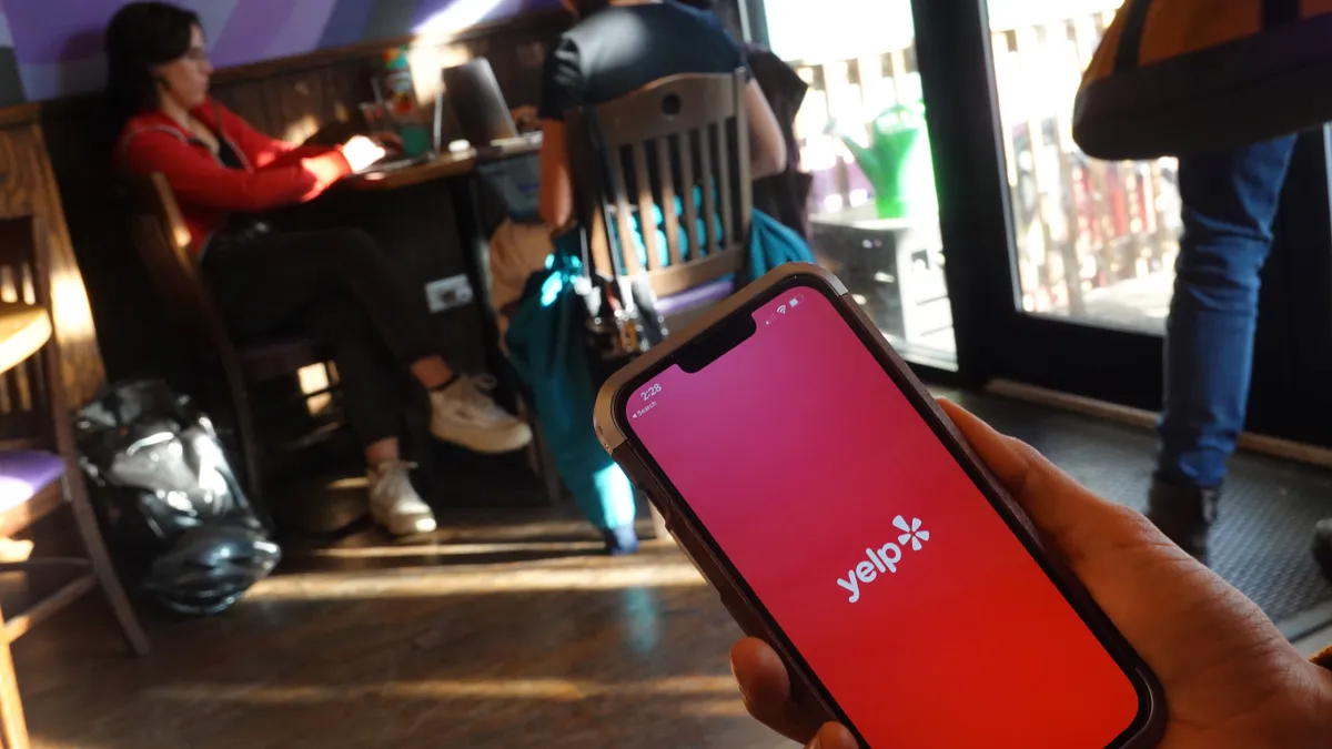 A person holds a smartphone in front of three people sitting at a table in a cafe.