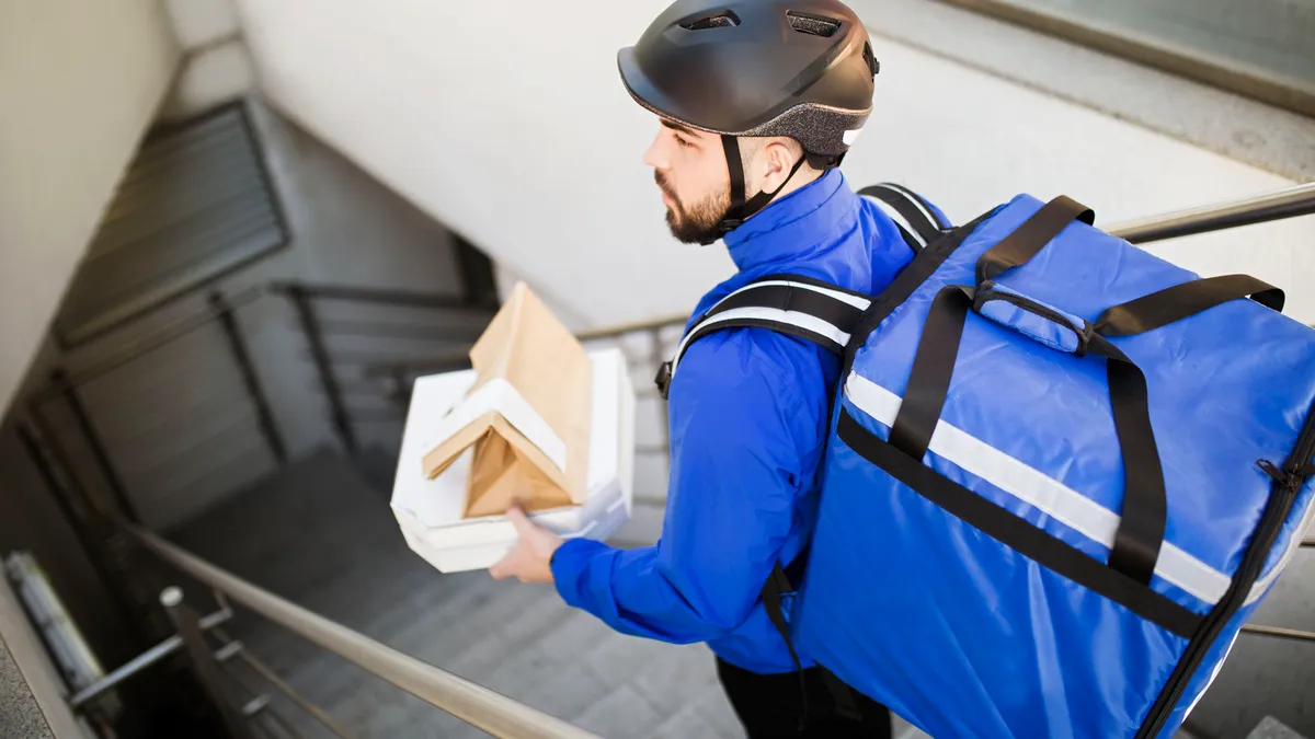 A young man delivers food down a flight of stairs.