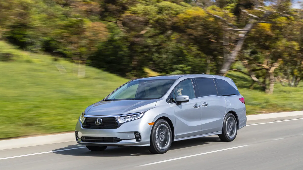 A silver 2022 Honda Odyssey minivan driving on a road with greenery in the background.