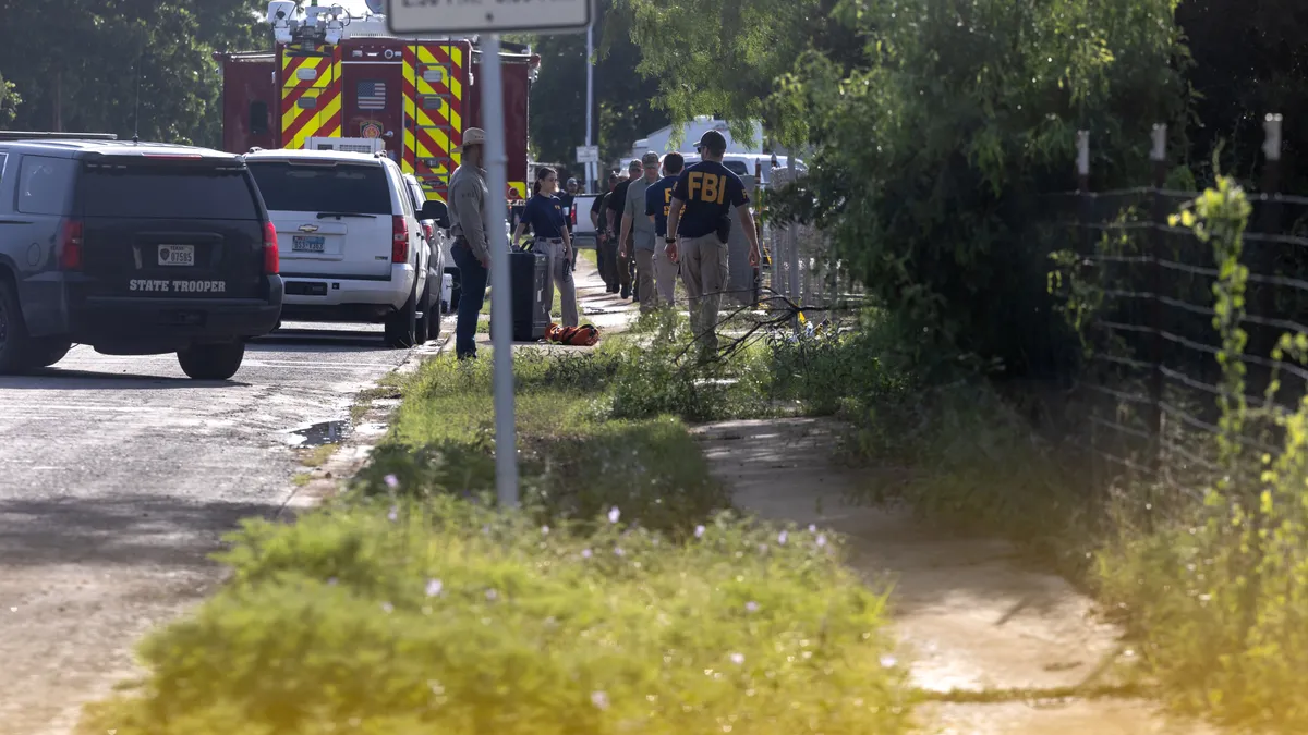 first responders walk on a side walk with vehicles to their left