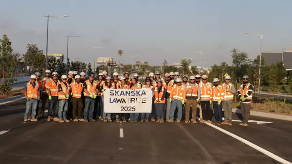 A group of construction workers pose for a photograph with a sign on a road.