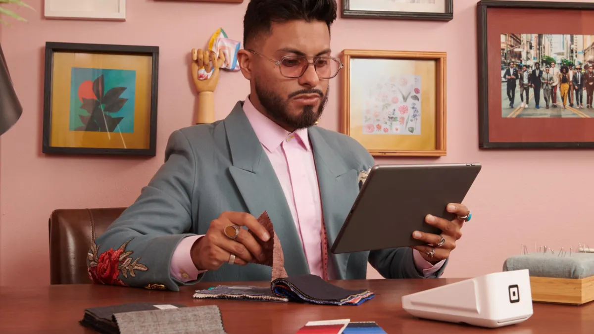 A seated down Retail Manager examines a tablet while a Square mobile device is placed on the desk they're at.