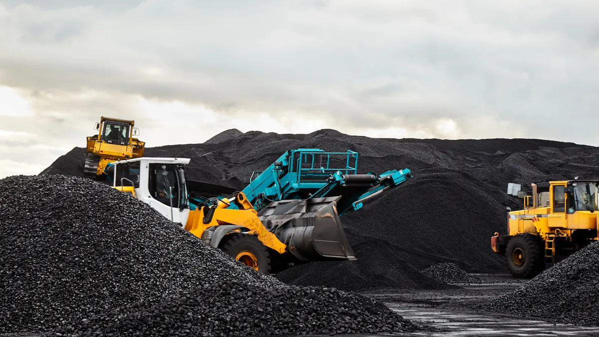 Caterpillar tractors collect black coal pile.